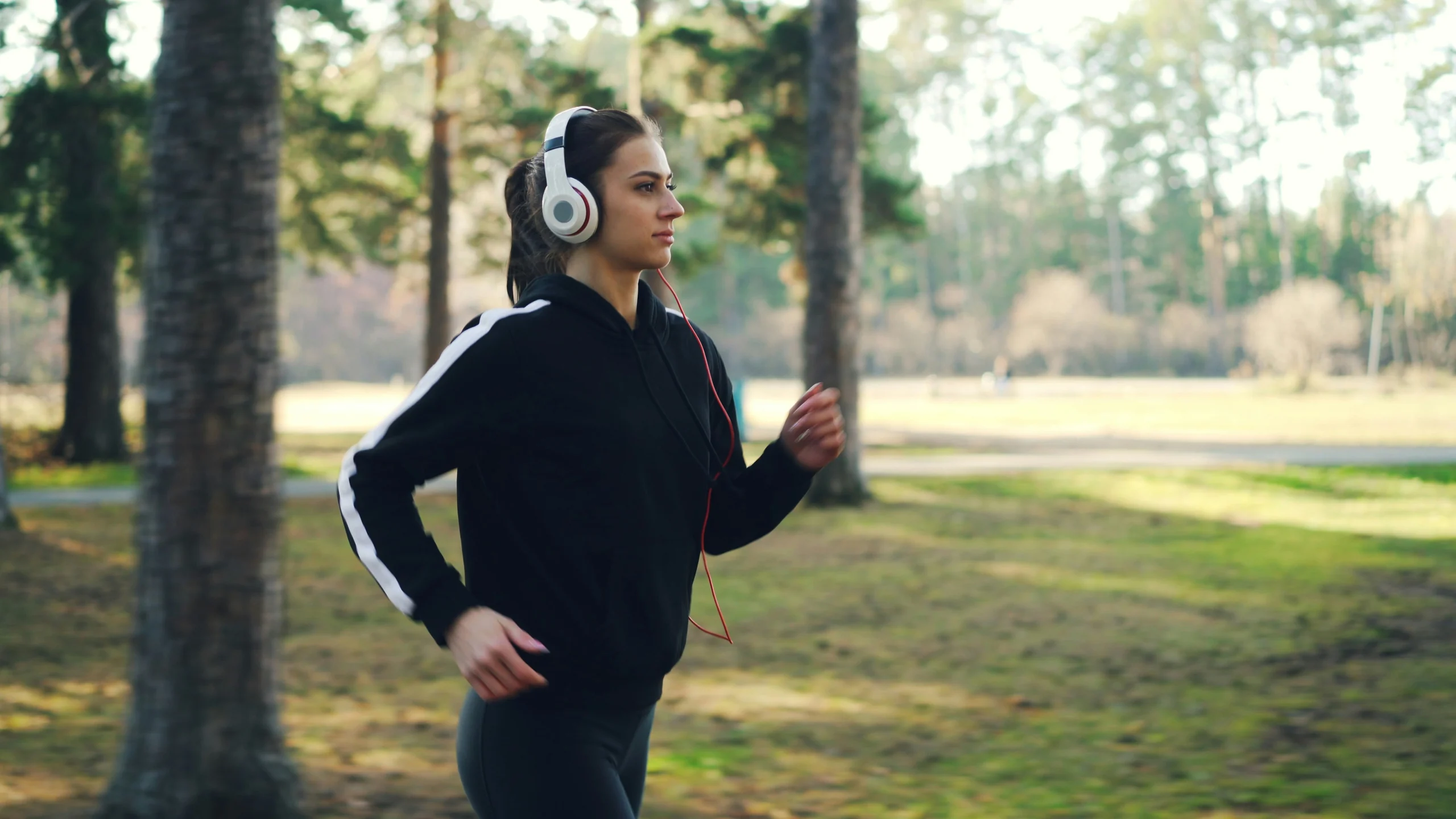 Woman with headphones jogging through a sunny park