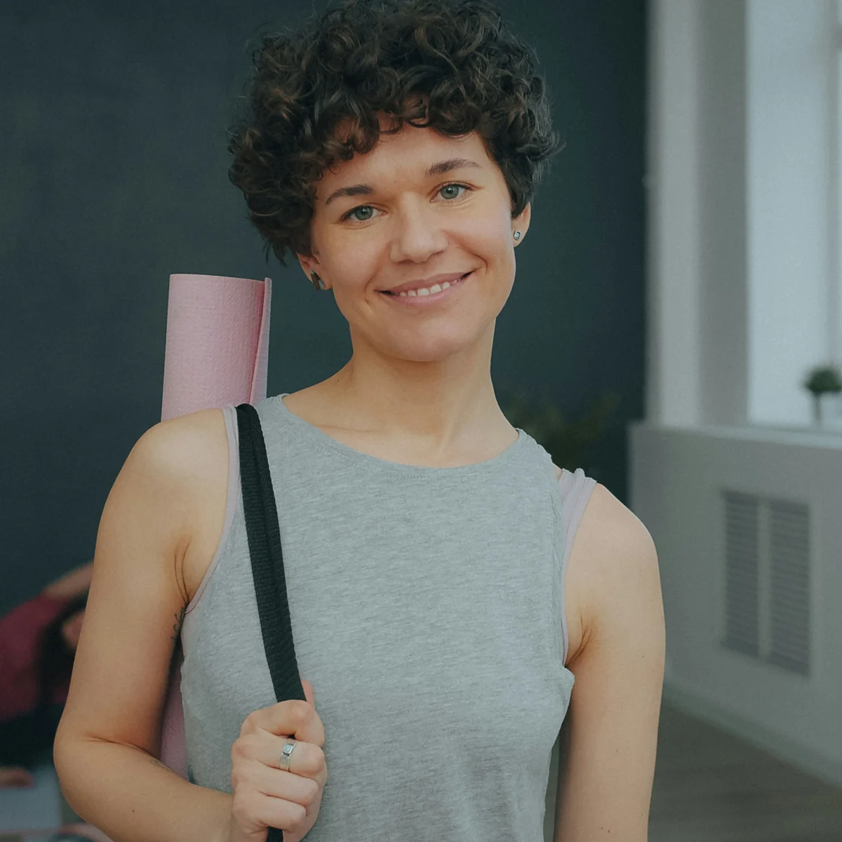 Smiling woman holding a rolled yoga mat in a studio
