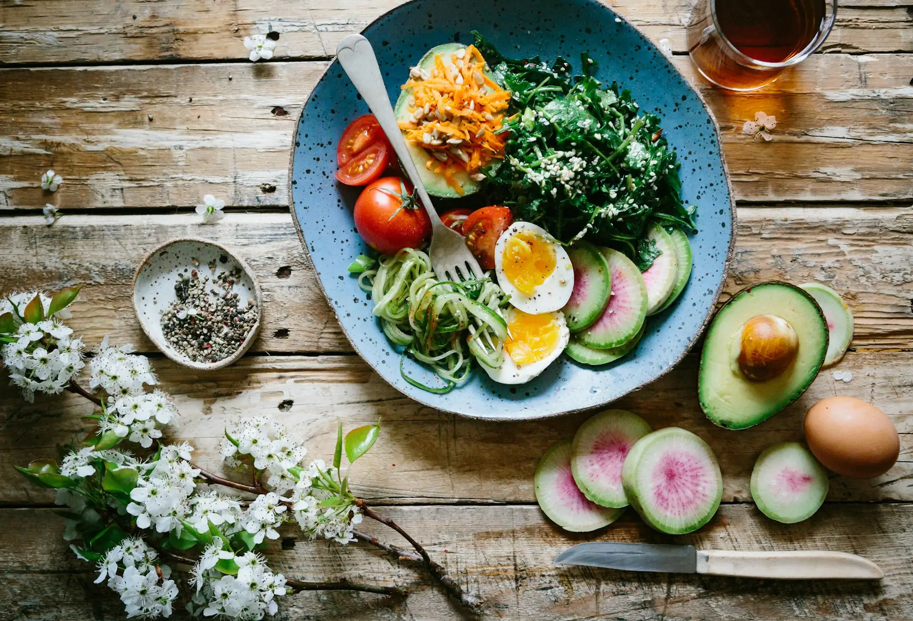 Bowl of eggs, avocado, and greens on a wooden table
